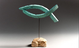 Escultura d'un peix de color verd sobre una base de pedra, obra d'Emili Armengol.