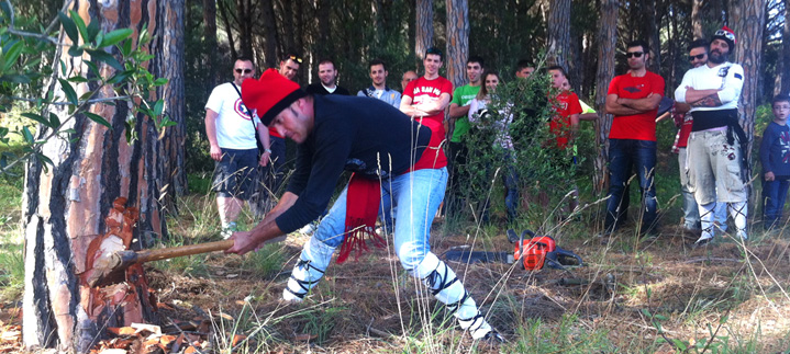 Un home talla el pi amb una destral mentre un grup de participants ho observa al bosc.