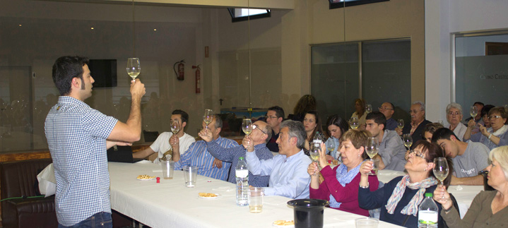 Una persona dreta alça la copa i s'adreça als assistents asseguts a les taules del tast de vins.