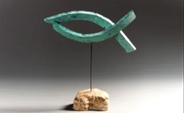 Escultura d'un peix de color verd sobre una base de pedra, obra d'Emili Armengol.