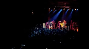 Concert nocturn: el públic omple la plaça davant d'un escenari il·luminat de blau.
