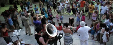 Una banda de metalls toca al mig d'una plaça envoltada de públic.