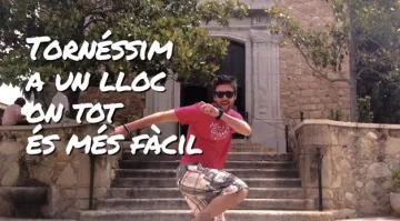 Fotograma del vídeo de la Festa Major 2012: una persona salta davant d'una escalinata de pedra, amb el text «Tornéssim a un lloc on tot és més fàcil».