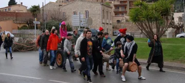 Una colla estira el carro amb el pi pel carrer, seguida per un grup de veïns.