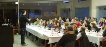 Sala plena amb taules parades per al tast de vins; una persona dreta s'adreça als assistents.