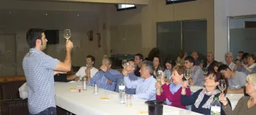 Una persona dreta alça la copa i s'adreça als assistents asseguts a les taules del tast de vins.